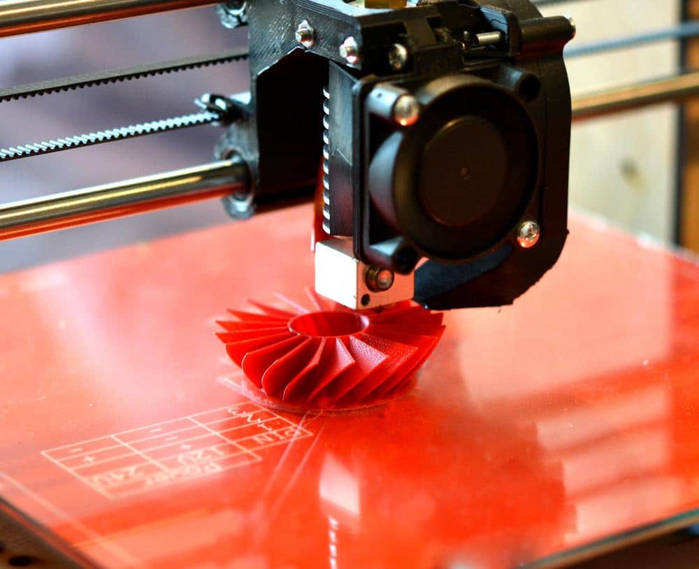 FDM 3D printer printing a red turbine part layer by layer on a heated bed
